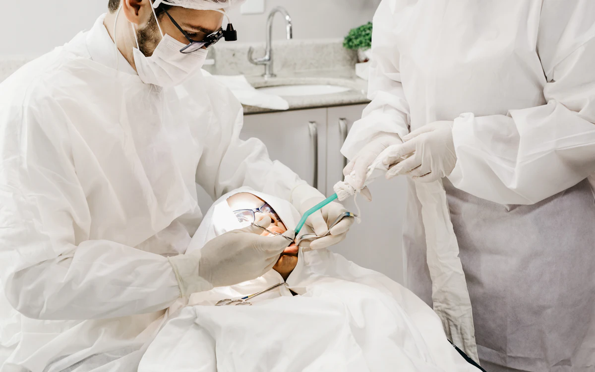 Dois profissionais de odontologia, de avental e óculos de proteção, durante um procedimento